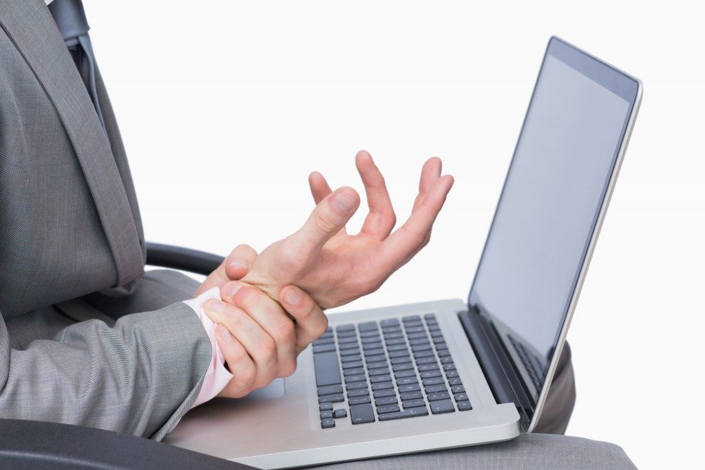Close-up of business man with wrist pain while using laptop over white background