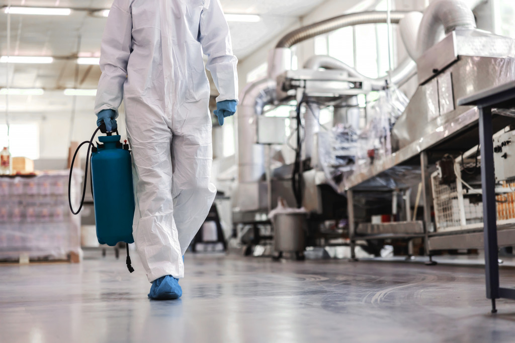 Worker in protective uniform carrying sprayer with disinfectant and walking around food factory. Corona virus outbreak concept.