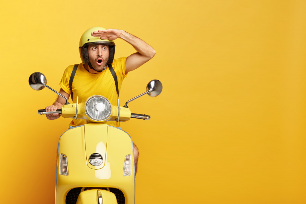 Stupefied male motorbike driver in ptotective helmet, keeps hand near forehead