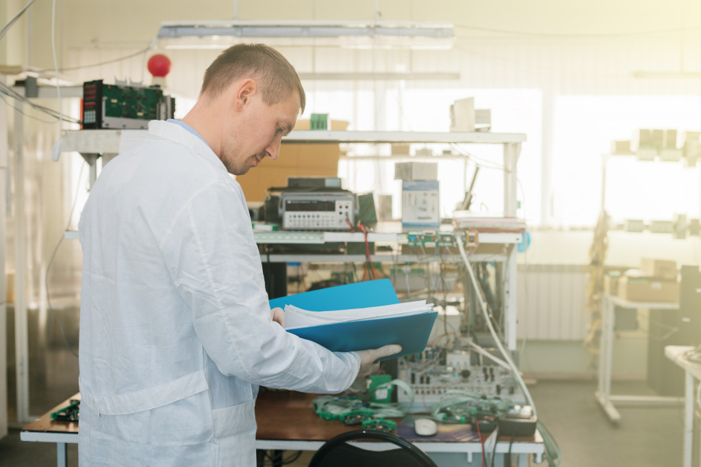 a male wearing a lab gown in a manufacturing facility holding paperwork