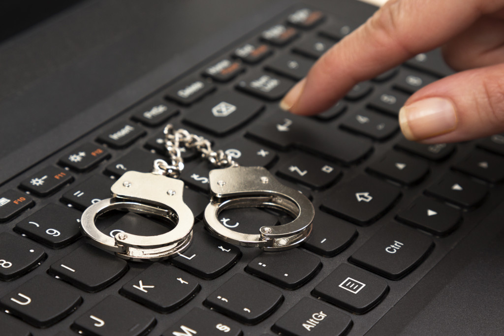 Small handcuffs on computer keyboard and female hand pressing the enter key