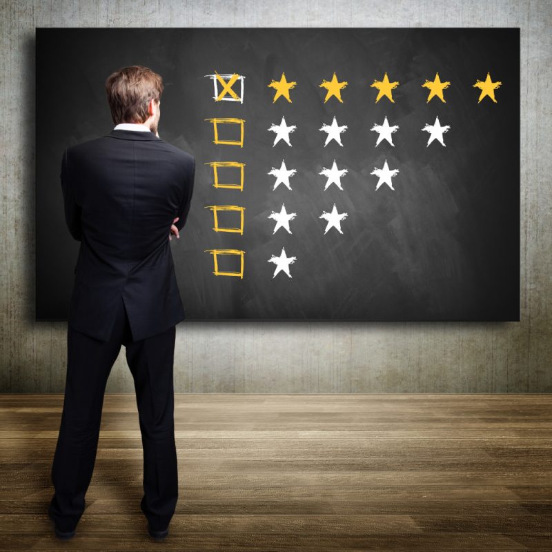 A businessman looking at a marked 5-star rating drawn on a blackboard